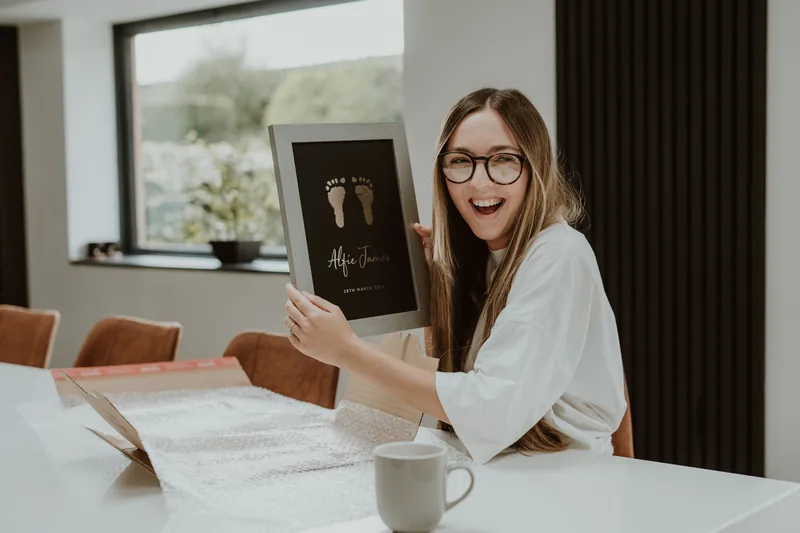 A customer smiling as she unboxes her framed foil footprint keepsake
